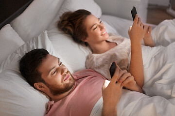 Image showing couple using smartphones in bed at night