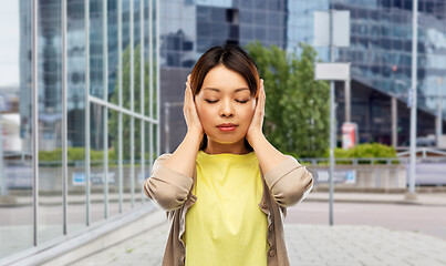 Image showing asian woman closing ears by hands on city street