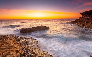 Image showing Sunrise over the ccean with some foreground rocks of eroded sand