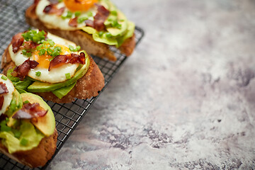 Image showing Breakfast concept. Tasty delicious homemade toasts with fried egg, bacon, avocado, lettuce and chive