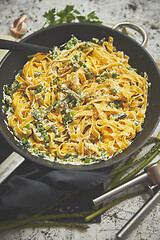 Image showing Tagliatelle pasta with ricotta cheese sauce and asparagus served on a black iron pan