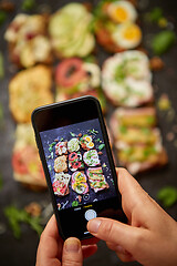 Image showing Woman making a photo with a smartphone of assortment of home made sandwiches with various toppings