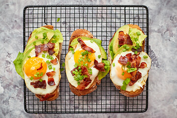 Image showing Tasty delicious homemade toasts with fried egg, bacon, avocado, lettuce and chive. Served on grill