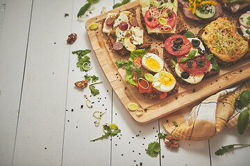 Image showing Tasty, homemade small sandwiches with various ingredients served on wooden chopping board