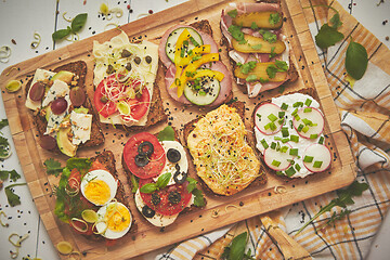 Image showing Tasty, homemade small sandwiches with various ingredients served on wooden chopping board