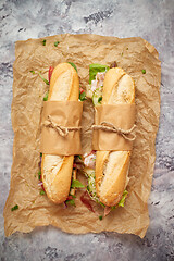 Image showing Sandwiches with ham, fresh vegetables and herbs served on brown baking paper over concrete backdrop