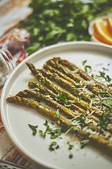 Image showing Delicious roasted asparagus served on white ceramic plate. With parmesan cheese, parsley and lemon.