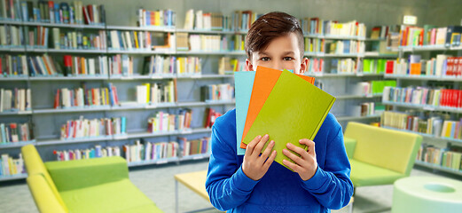 Image showing shy student boy hiding behind books at library