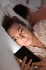 Image showing woman using smartphone while boyfriend is sleeping