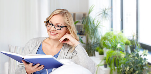 Image showing smiling woman reading book and sitting on couch