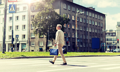 Image showing senior man with shopping bags walking on crosswalk