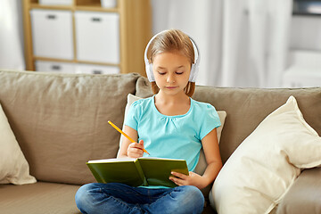 Image showing girl in headphones with diary on sofa at home