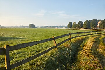 Image showing Green field with fence by a village