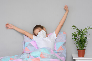 Image showing A recovering girl in a medical mask woke up in the morning and stretches herself in bed