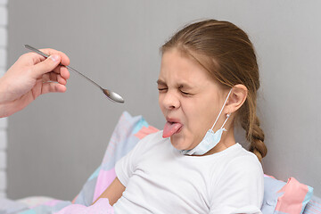 Image showing The girl frowns at the medicine given to her and pulled out her tongue