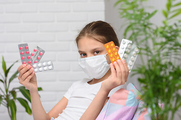 Image showing Girl holding in her hands a lot of pills in a pack, even in a medical mask in bed