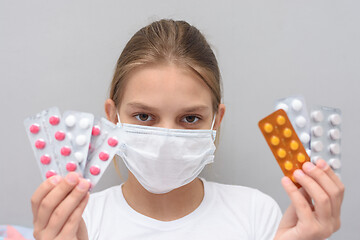 Image showing A girl with a medical mask on her face holds blisters with medicines