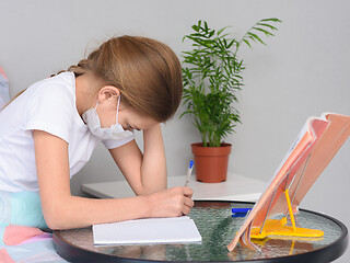 Image showing A girl in a medical mask does homework at a table in front of the bed