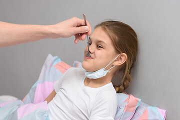 Image showing A sick girl is given medicine from a spoon in her mouth