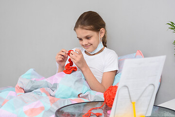 Image showing The sick girl in quarantine at home is engaged in needlework lying in bed.