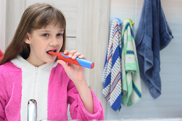 Image showing Ten year old girl brushes her teeth with an electric toothbrush in the bathroom