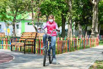 Image showing A ten-year-old girl in a medical protective mask rides a Bicycle