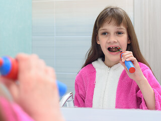 Image showing The girl looks in the mirror and brushes her teeth with an electric toothbrush