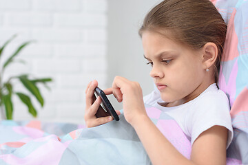 Image showing Girl playing on a cell phone while lying in bed