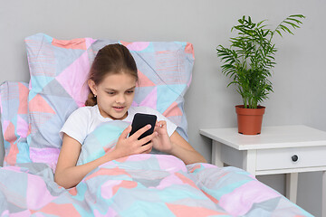 Image showing Girl communicates with friends online in a mobile phone while lying in bed.