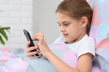 Image showing The girl lies in bed and plays in a mobile smartphone