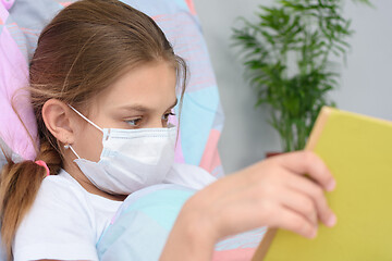 Image showing Girl reading a book while lying in bed in a hospital ward