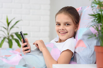 Image showing The girl plays in the mobile phone and looked happily into the frame.