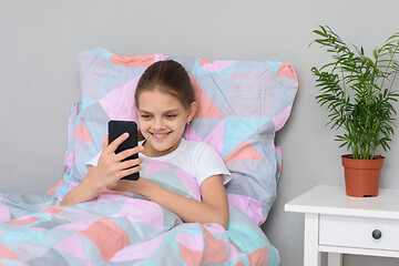 Image showing Happy girl lying in bed communicates on a mobile phone
