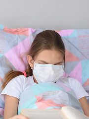 Image showing The sick girl decided to fall asleep while reading a book and pulled a medical mask over her face