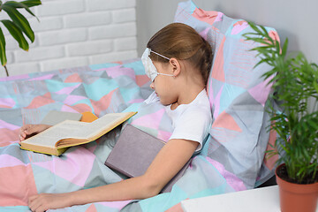 Image showing the girl fell asleep lying in bed and reading books, a medical mask is put on her eyes