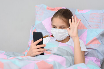 Image showing A sick girl lies in bed and communicates with friends online via video-telephone