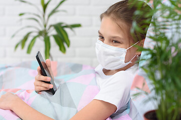 Image showing A recovering quarantined girl smiles and holds a mobile phone in her hands