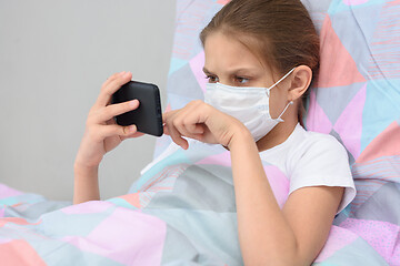 Image showing The quarantined girl lies in bed with a mobile phone