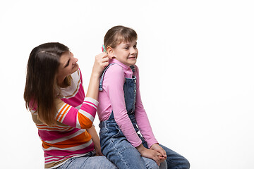 Image showing Girl sitting on moms lap, mom fun tugs at the girls ear