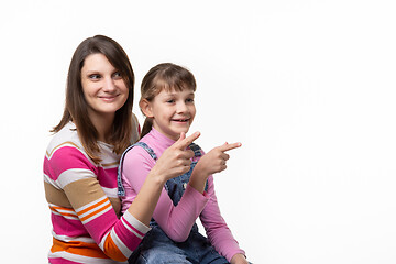 Image showing Girl sitting on moms lap and joyfully point a finger to an empty place