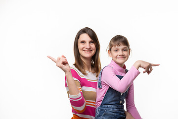 Image showing Cheerful mother and daughter point fingers in different directions, isolated on white background