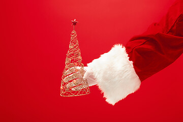 Image showing Hand of Santa Claus holding a toy christmas tree on red background