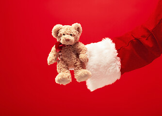 Image showing Hand of Santa Claus holding a gift on red background