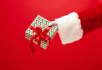 Image showing Hand of Santa Claus holding a gift on red background