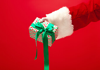 Image showing Hand of Santa Claus holding a gift on red background