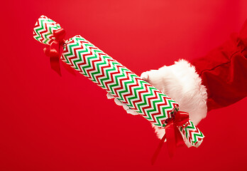 Image showing Hand of Santa Claus holding a gift on red background