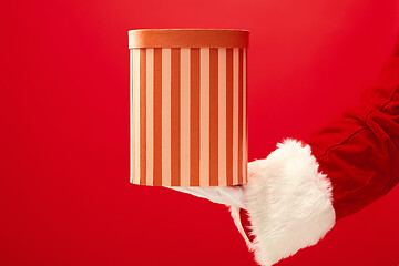 Image showing Hand of Santa Claus holding a gift on red background