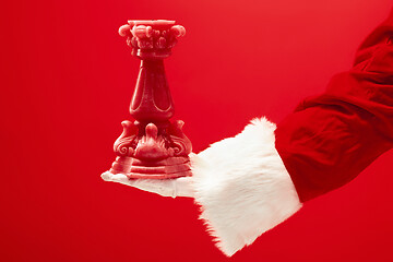 Image showing Hand of Santa Claus holding a toy Christmas candle on red background