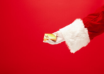 Image showing Hand of Santa Claus holding a gift on red background