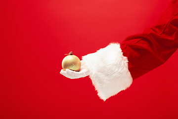 Image showing Hand of Santa Claus holding a toy Christmas decorations on red background